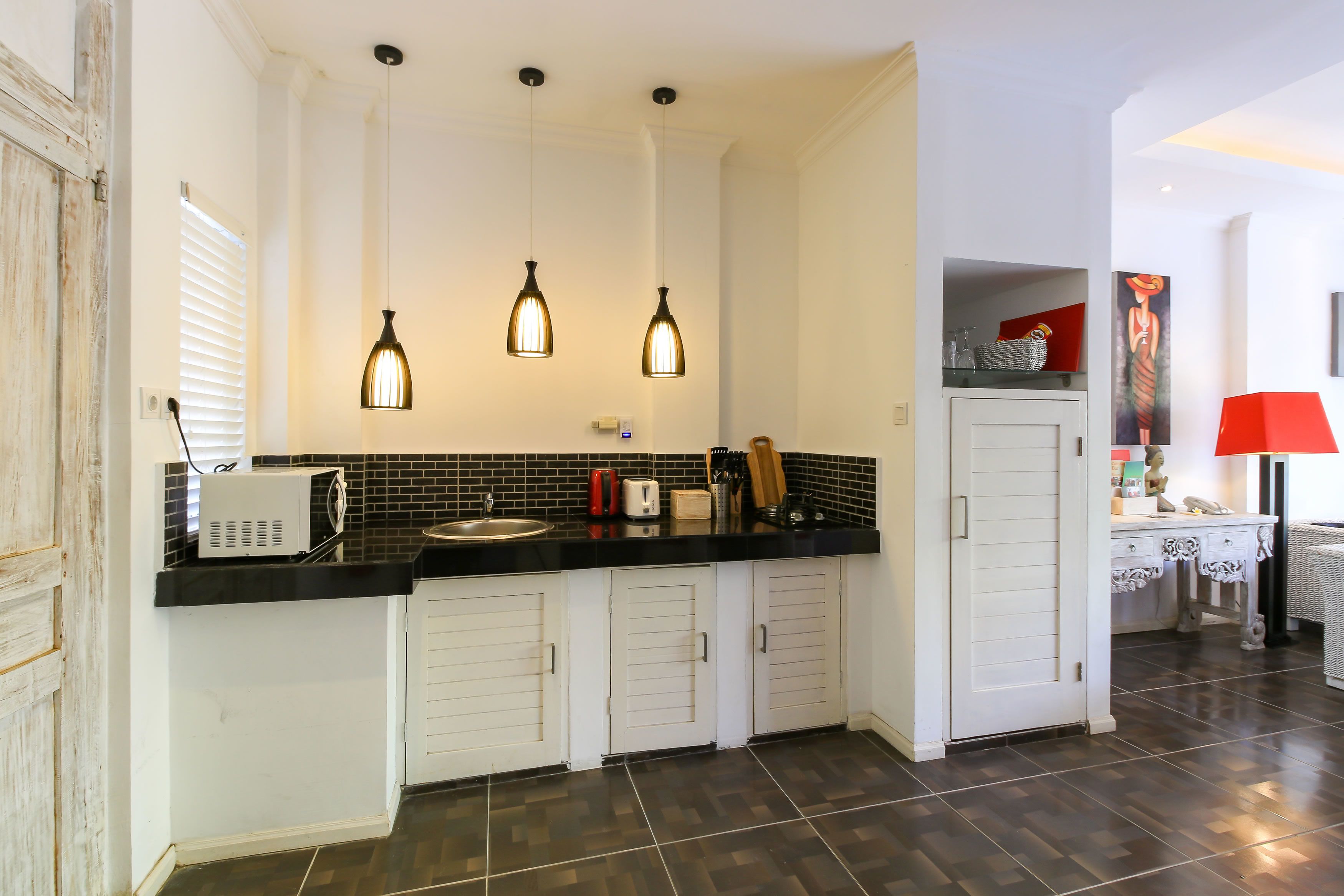 A kitchen with a black countertop, white cabinets, and three pendant lights.