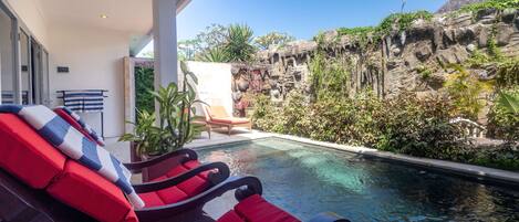 A pool area with red lounge chairs, a small table, and a potted plant.