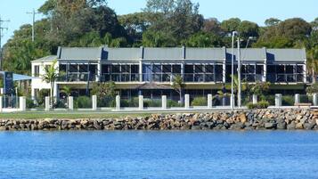 A waterfront hotel with a modern architectural design, featuring multiple balconies and a stone retaining wall.