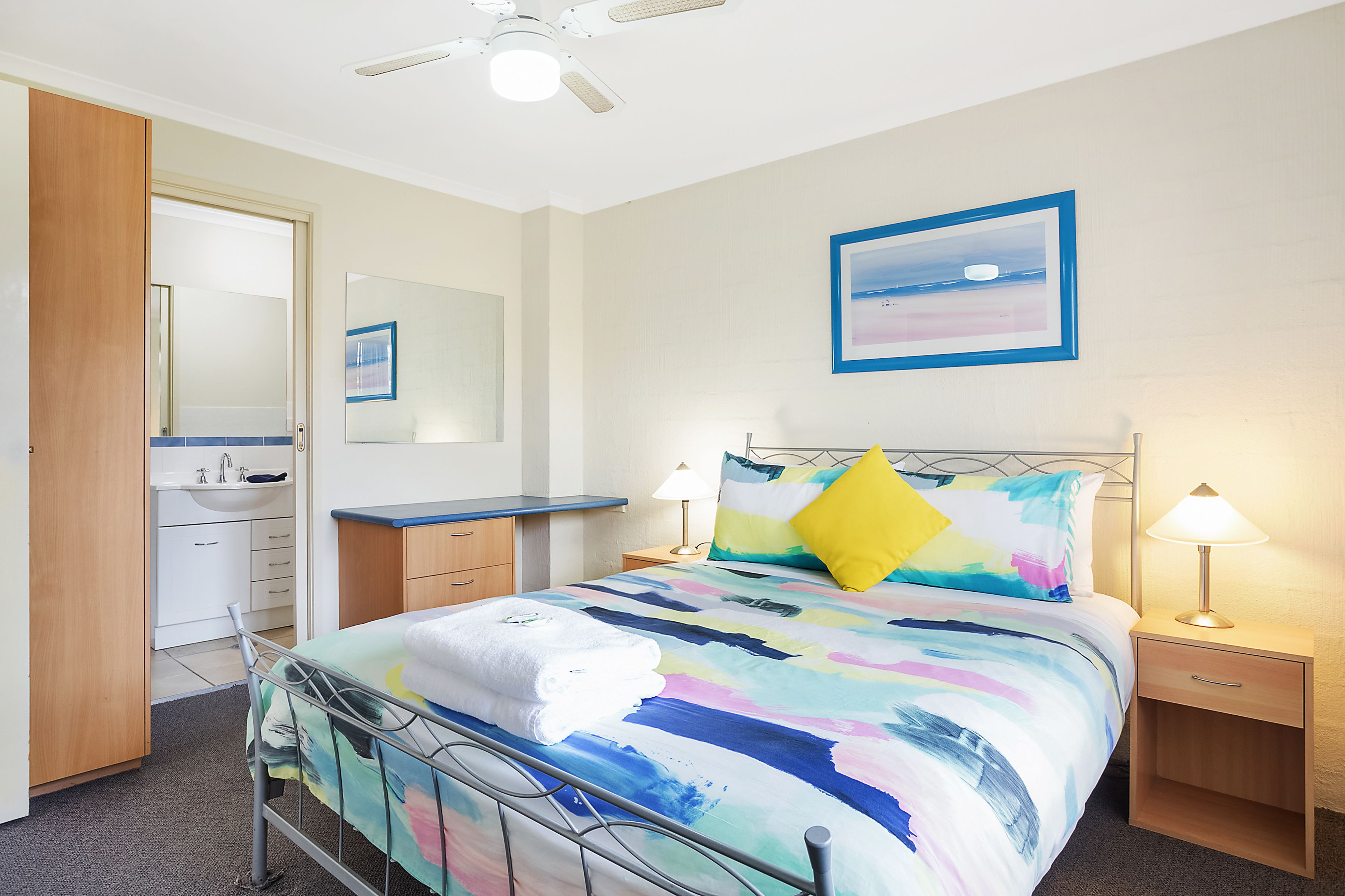 A neatly arranged bedroom with a bed, bedside tables, a nightstand, a mirror, and a bathroom area.