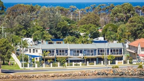 Un hôtel situé sur la côte, avec un bâtiment à deux étages, un espace extérieur aménagé et couvert, et une vue sur la mer.