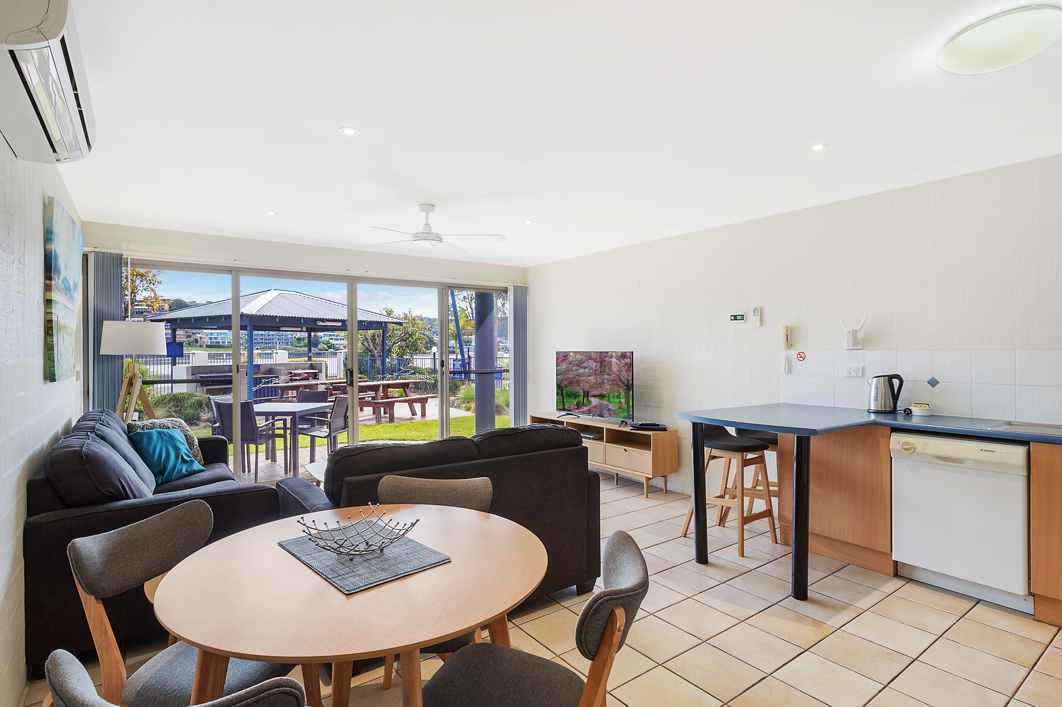 A modern kitchen with a dishwasher, a dining area with a round table and chairs, and a large sliding glass door leading to an outdoor patio.