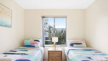 Una camera da letto con due letti, un comodino con una lampada e una finestra che si affaccia su edifici e alberi.