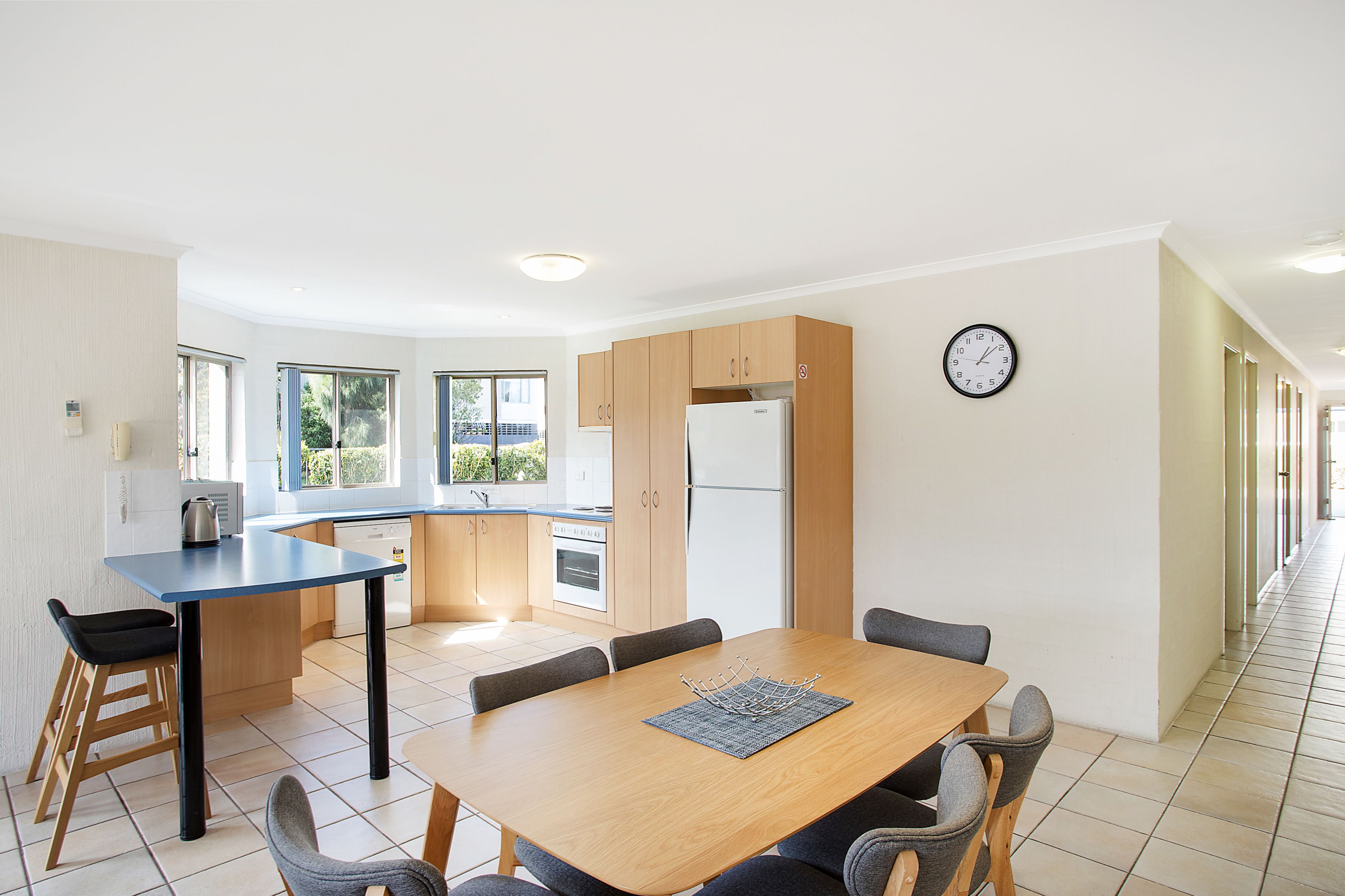 Una cocina moderna con comedor, que incluye una mesa de madera, sillas y un reloj en la pared.