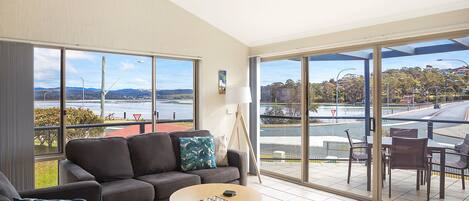 A spacious living room with a large window, a sofa, a coffee table, and a view of a body of water and hills.
