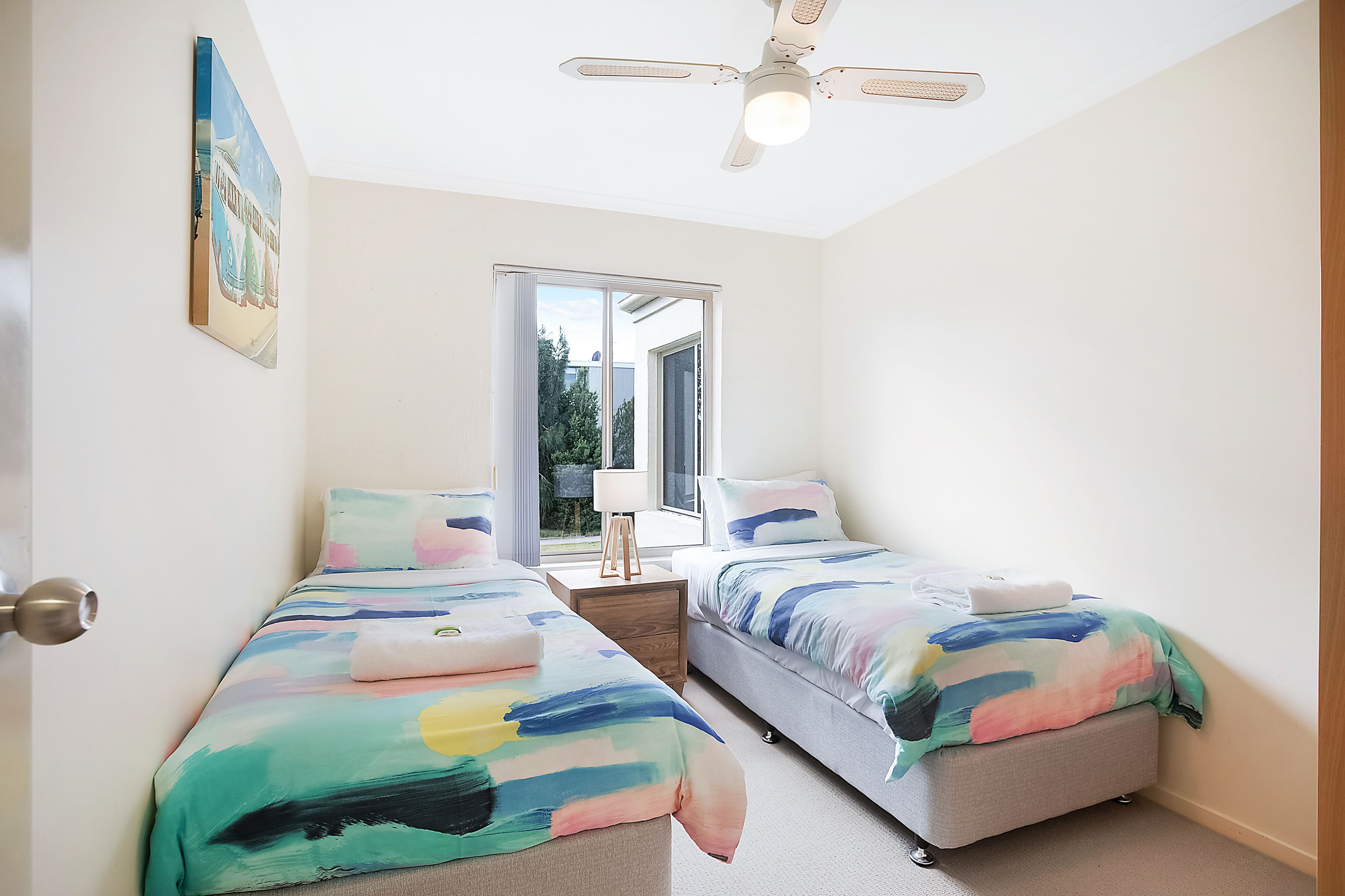 Une chambre avec deux lits, un ventilateur de plafond, une fenêtre et une porte.