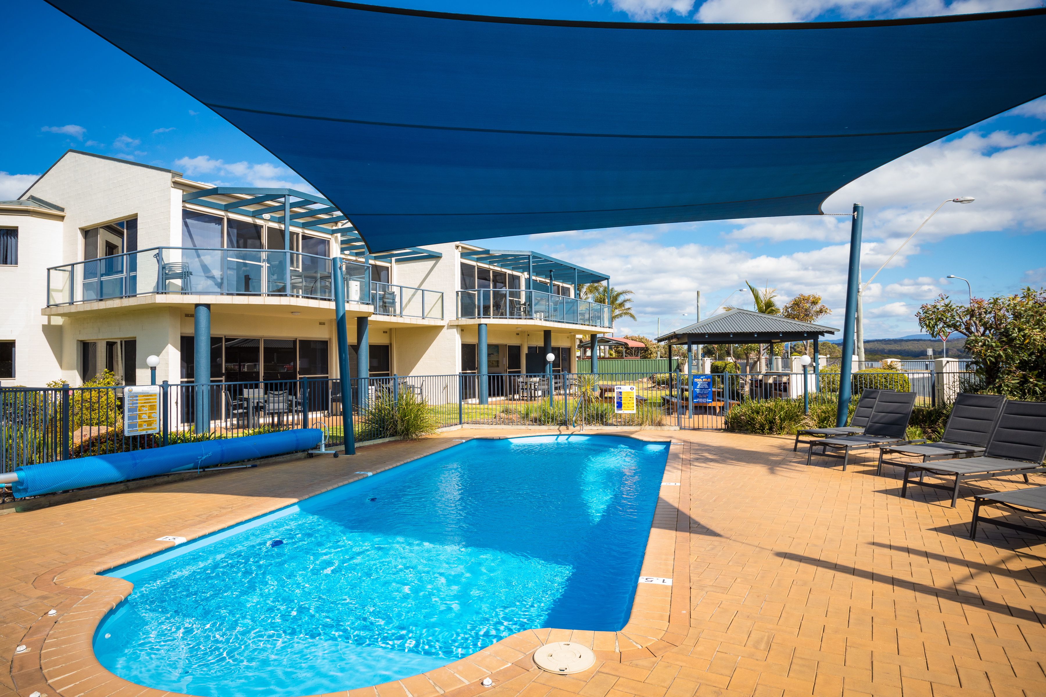 Una piscina con ombrellone, lettini e un edificio con balconi.