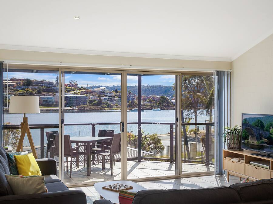 A modern living room with a large sliding glass door leading to a balcony overlooking a lake and town.