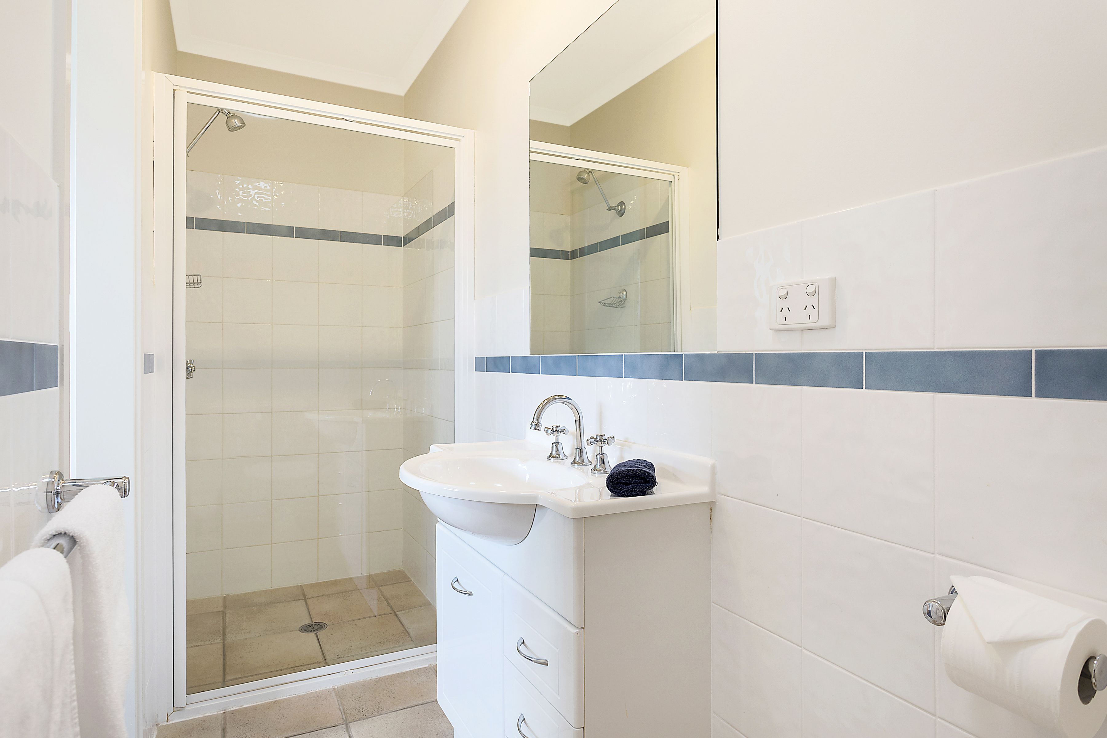 A bathroom with a glass shower enclosure, a white sink with a towel, and a mirror above it.