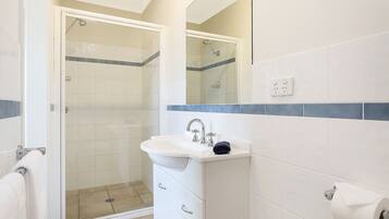 A bathroom with a glass shower enclosure, a white sink with a towel, and a mirror above it.