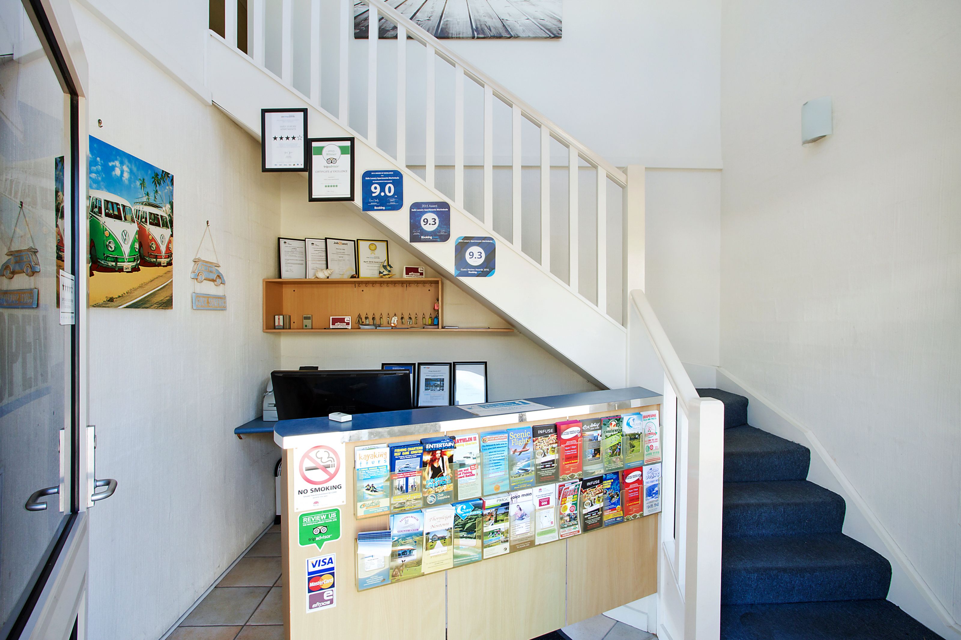 Un comptoir d’accueil, un escalier avec une rampe blanche et divers affiches d’information accrochées au mur.