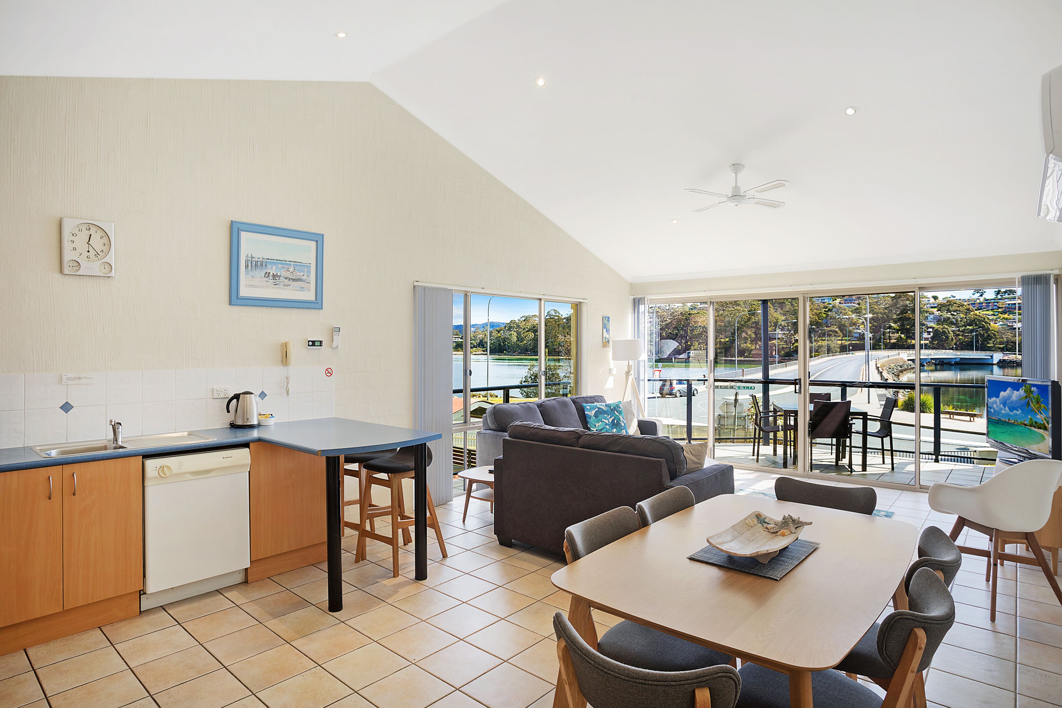 A modern kitchen with a dishwasher, a dining area with a table and chairs, and a large window offering a view of the outdoors.
