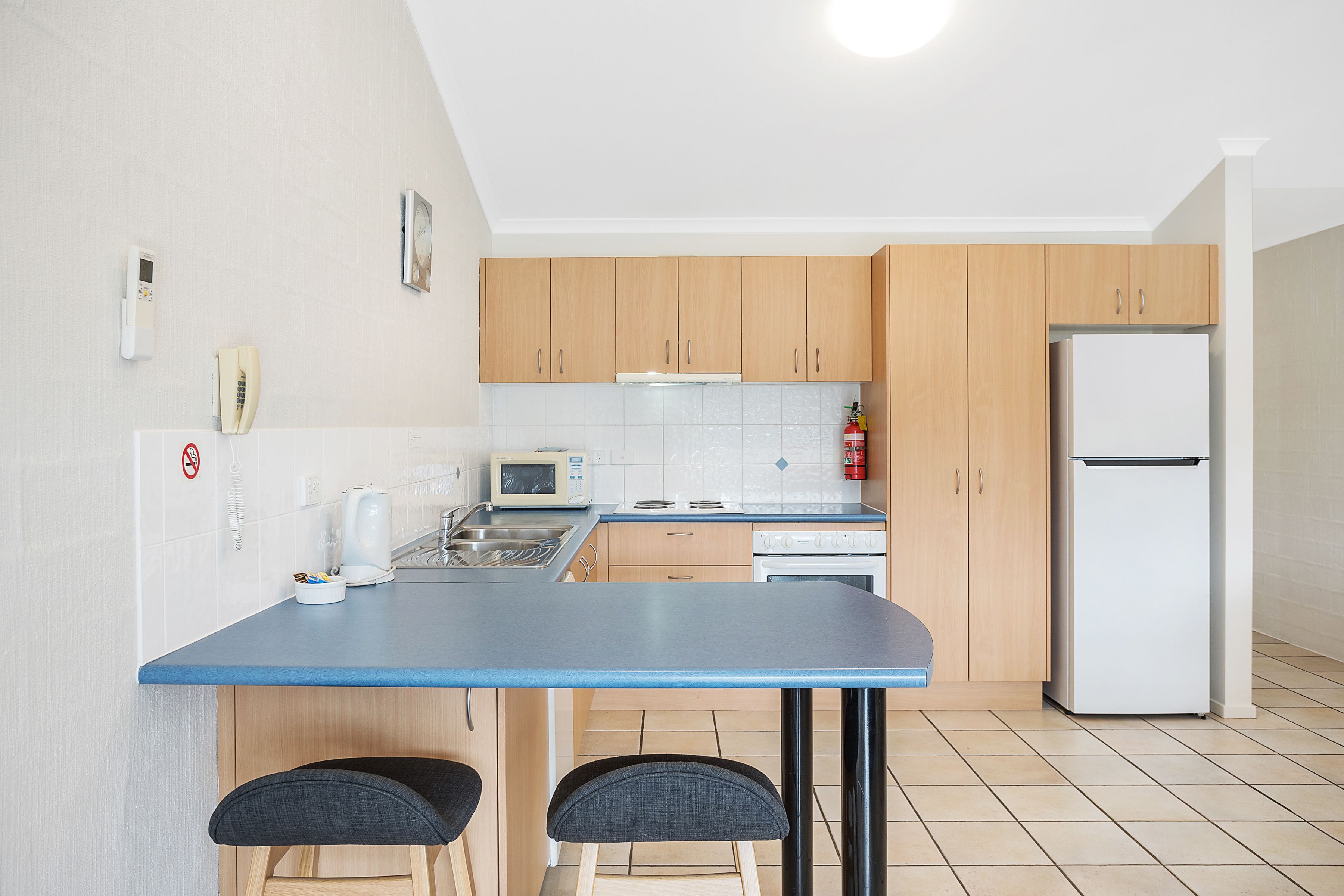 Une cuisine de taille réduite avec un plan de travail bleu, des placards en bois, un four à micro-ondes, une cuisinière et un réfrigérateur.