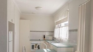 A compact kitchen with a dining area, white cabinetry, a small oven, and a window with curtains.