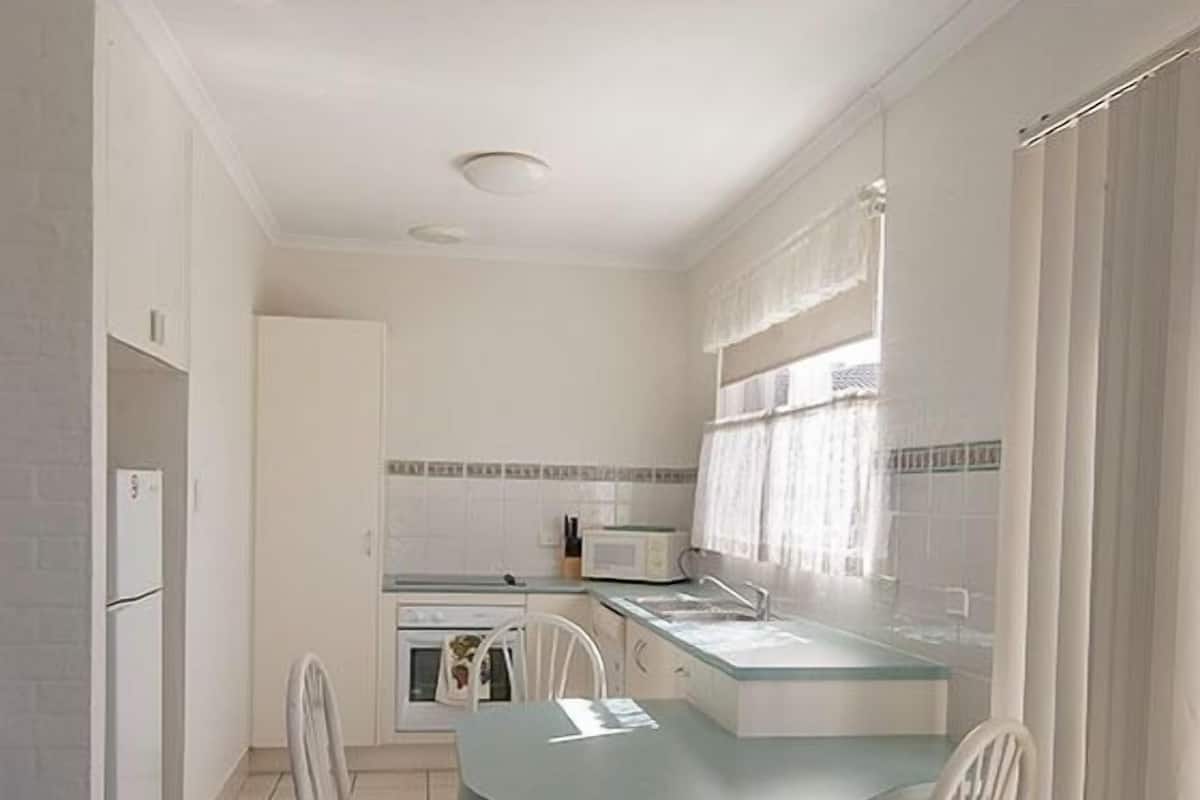 A compact kitchen with a dining area, white cabinetry, a small oven, and a window with curtains.