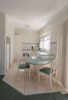 Cocina compacta con comedor, muebles de cocina blancos, horno pequeño y ventana con cortinas.