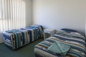 A room with two beds, each with striped bedding, a small bedside table, and a window with blinds.