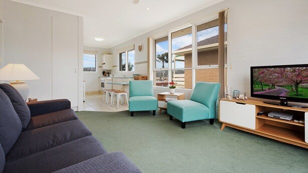 A modern living room with a sofa, two armchairs, a TV, and a kitchen in the background.
