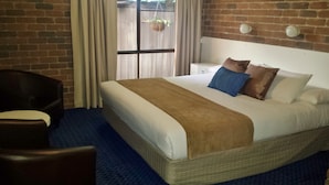Habitación de hotel con una cama grande, una silla, una mesita de noche y una ventana con cortinas.