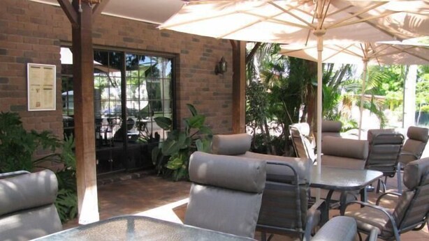 Un área de patio al aire libre con mesas y sillas de metal, rodeada de muros de ladrillo y plantas en macetas.