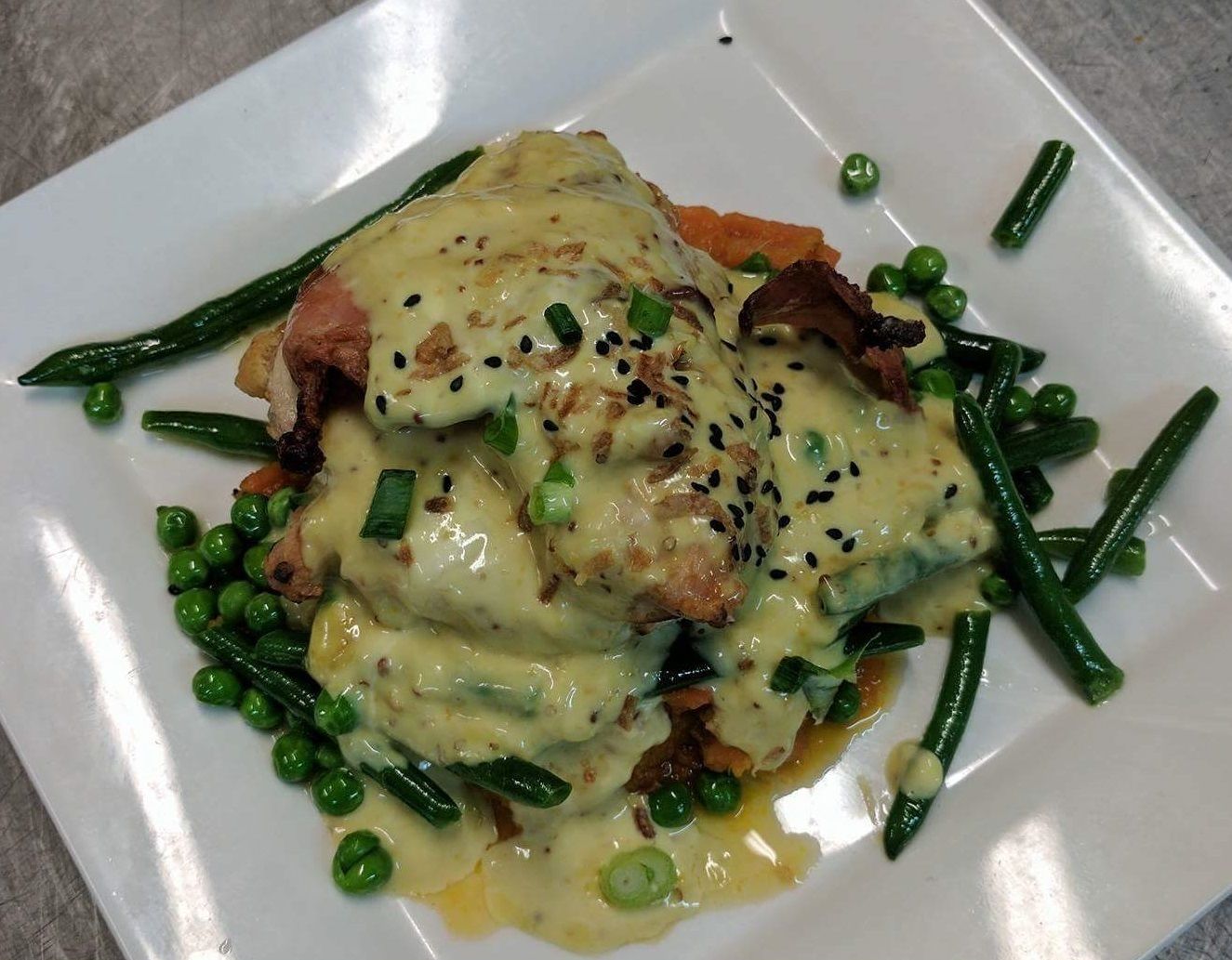Ein Teller Essen mit cremiger Soße, grünen Bohnen und einem Fleischstück.