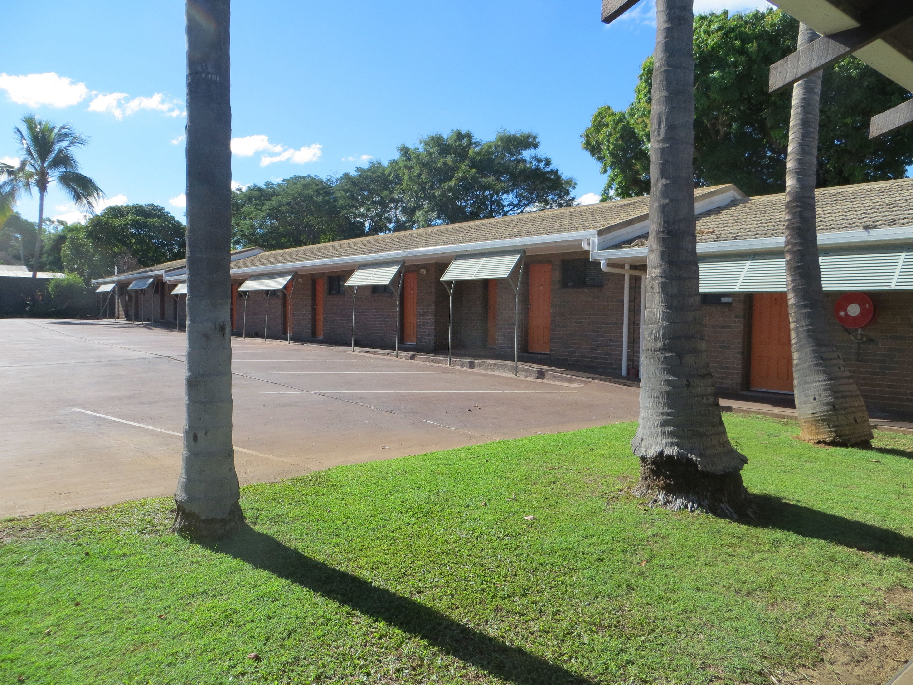 A row of single-story buildings with a flat roof, likely a motel or inn, with a parking lot in front.