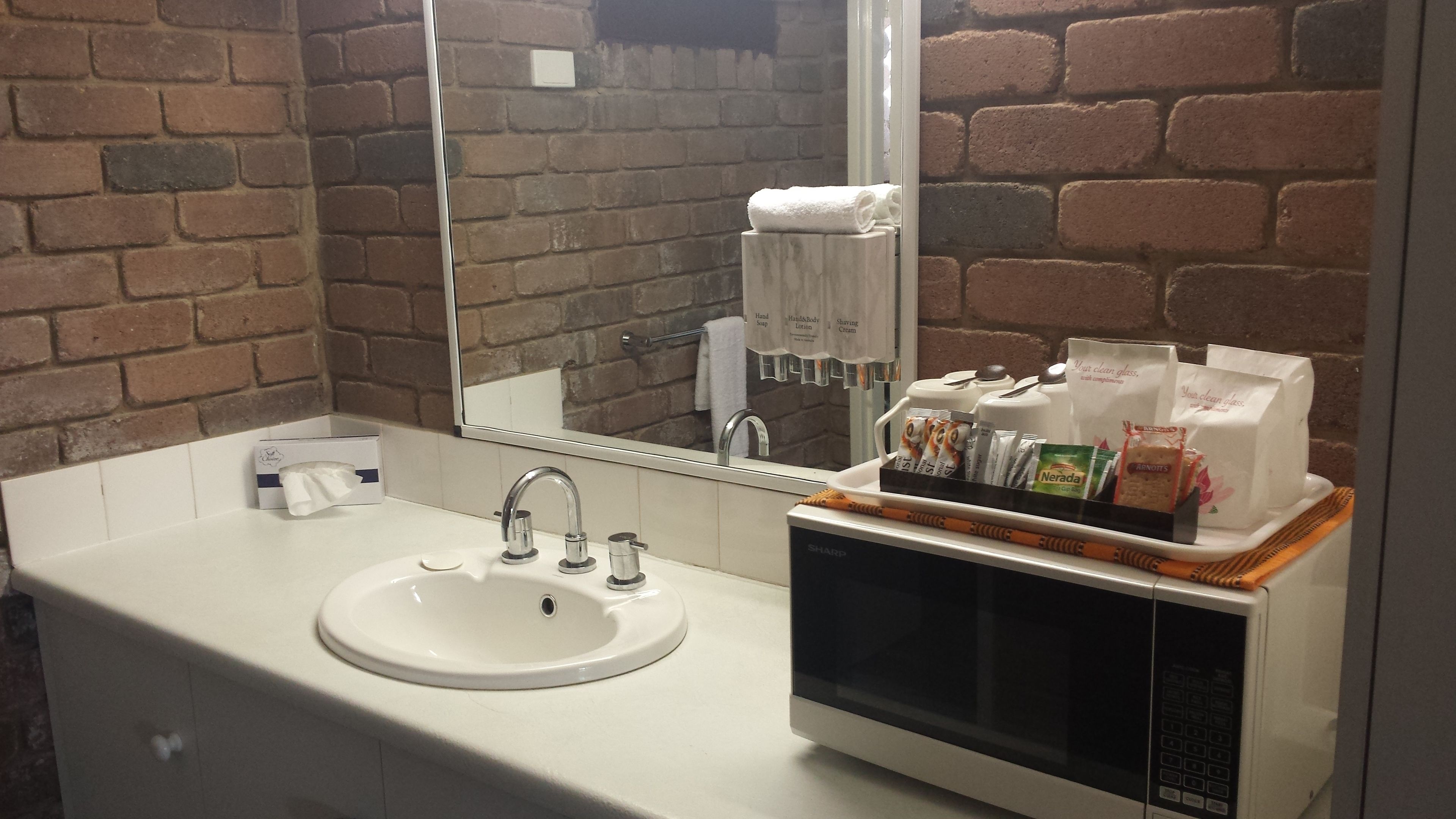 Un baño con lavamanos blanco, un espejo, toallero y repisa con artículos de aseo.