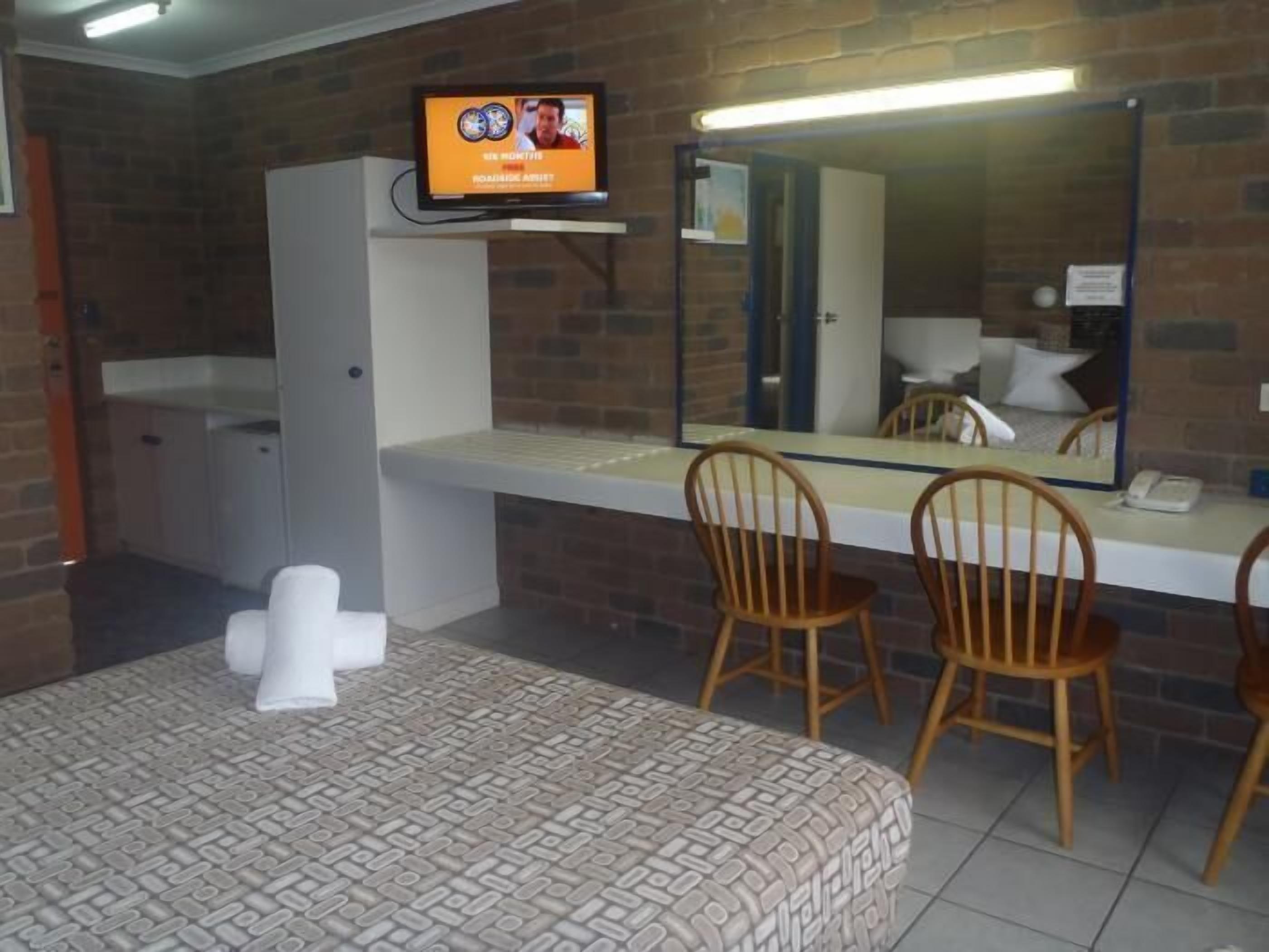 Ein Hotelzimmer mit einem Bett, einem an der Wand befestigten Fernseher, einem Spiegel über dem Bett und einem kleinen Tisch mit Stühlen.