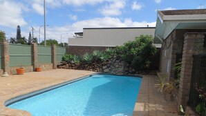 Una piscina rectangular con agua azul cristalina, rodeada por un patio de ladrillo y un muro de piedra con plantas.