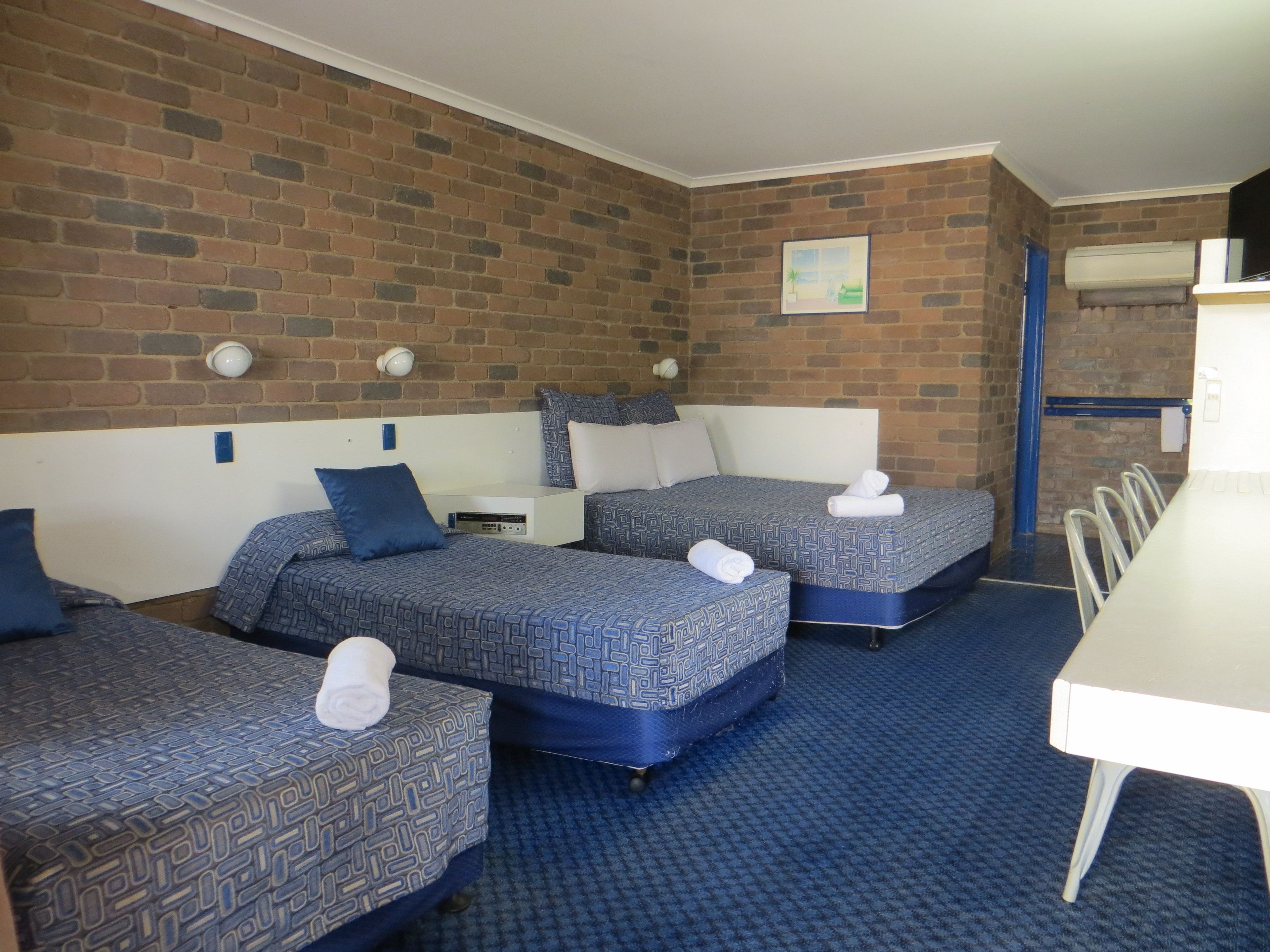 Habitación de hotel con tres camas, una mesa blanca y una pared de ladrillo.