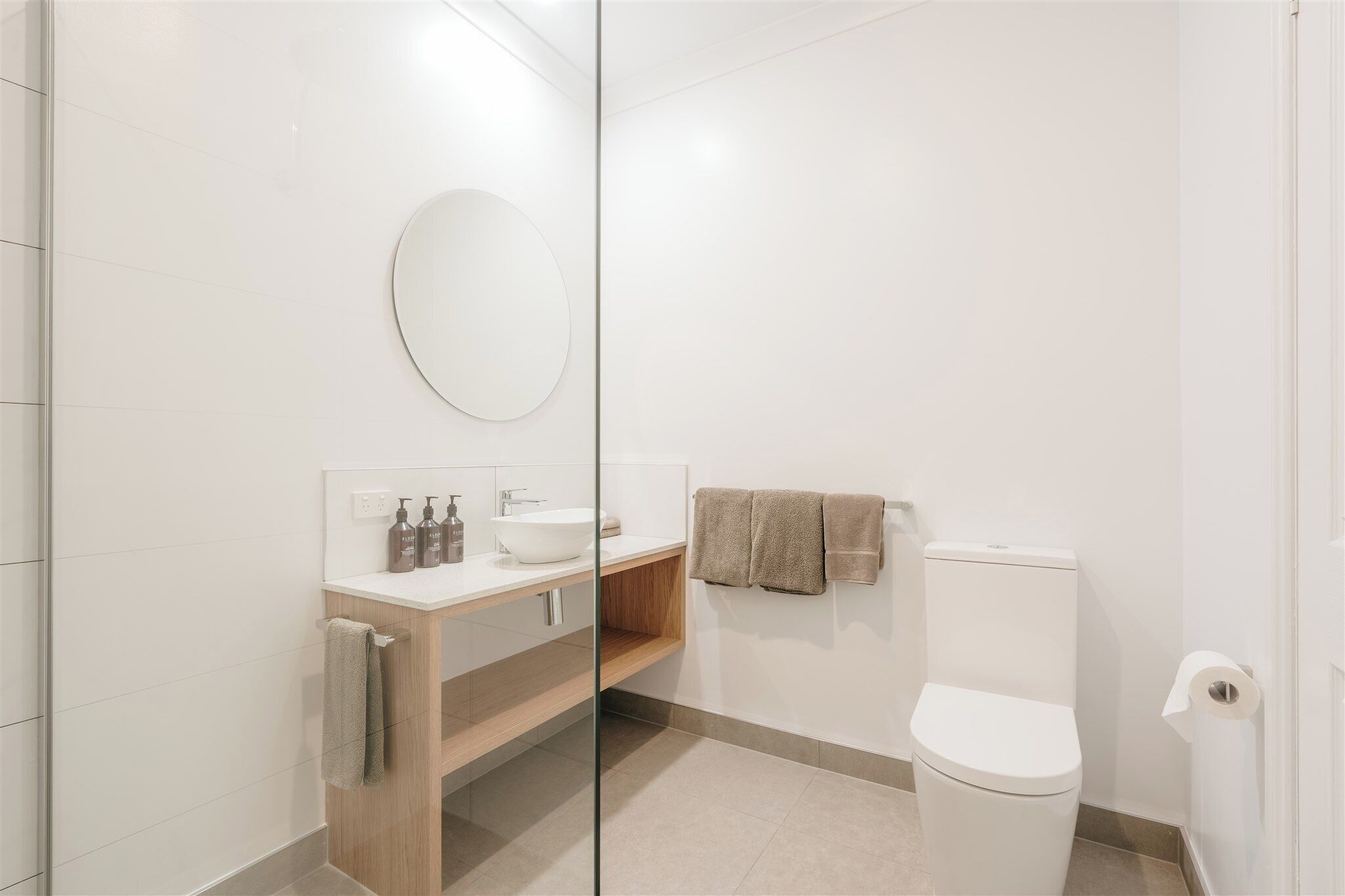 Un baño moderno con lavamanos, espejo y retrete blancos.