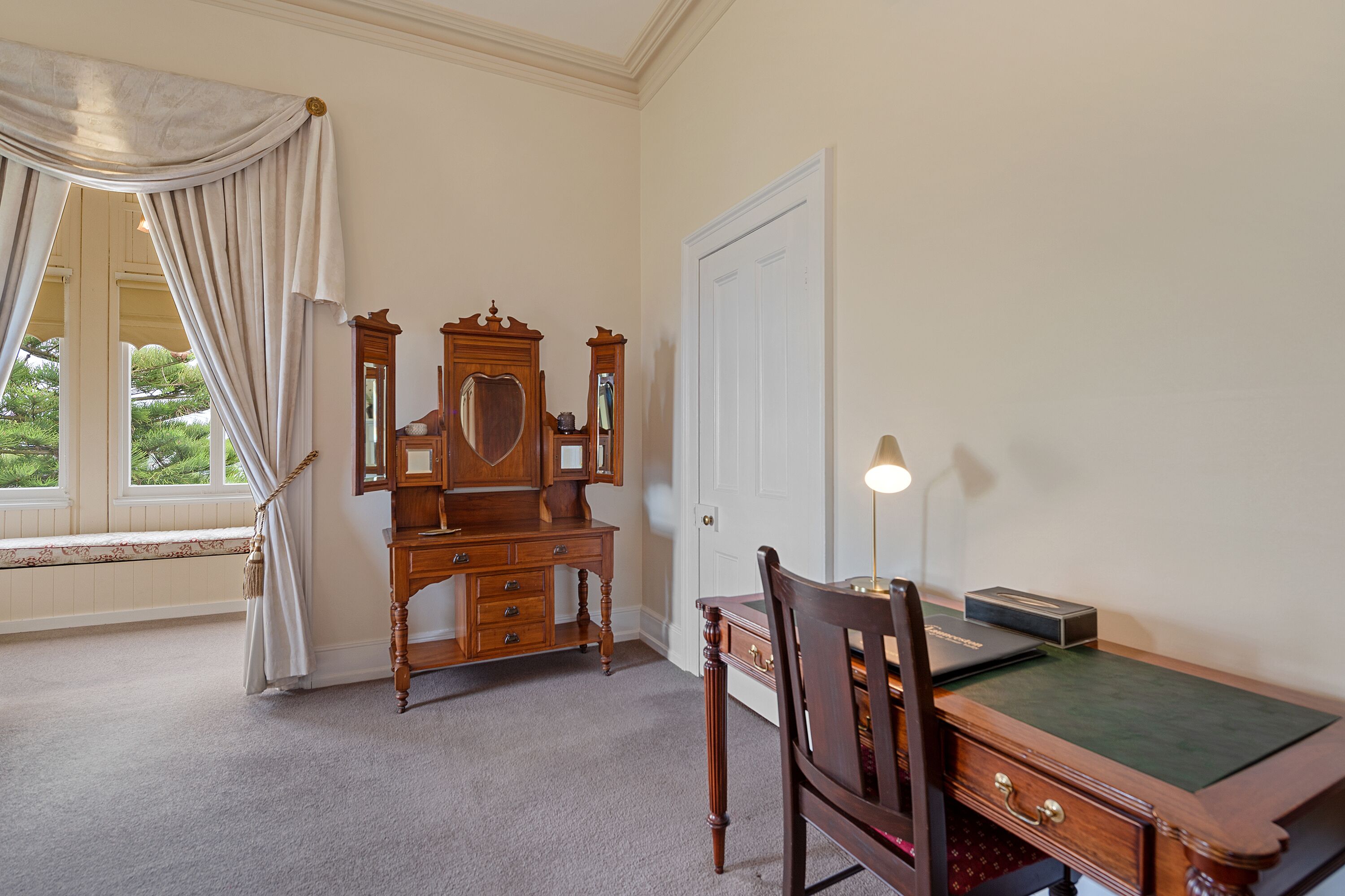 Une pièce comprenant un bureau en bois, une chaise, un miroir, une lampe et une porte.