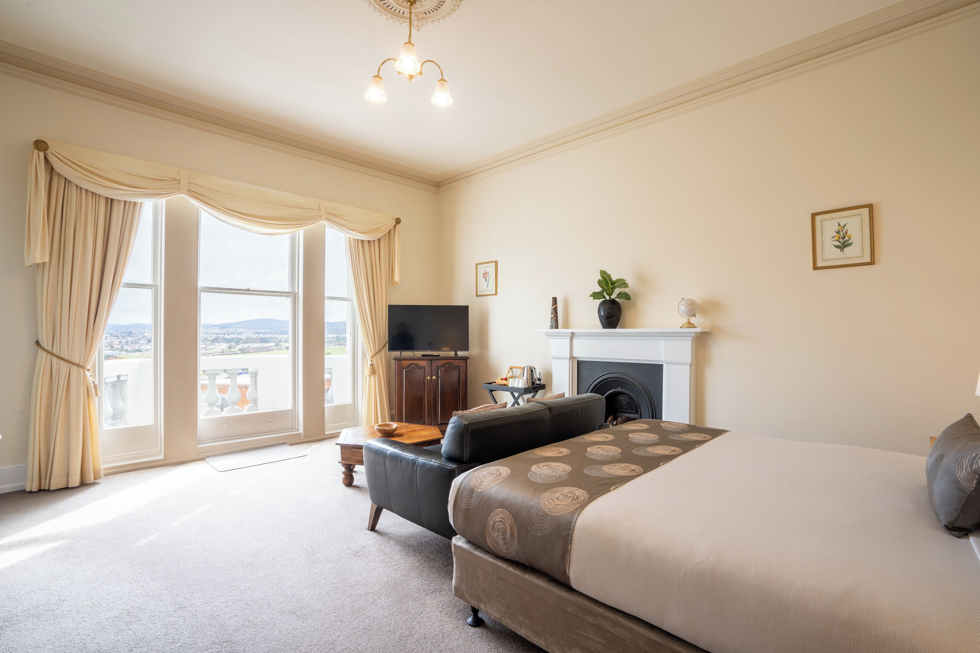 A bedroom with a large bed, a television, a fireplace, and a balcony with curtains.