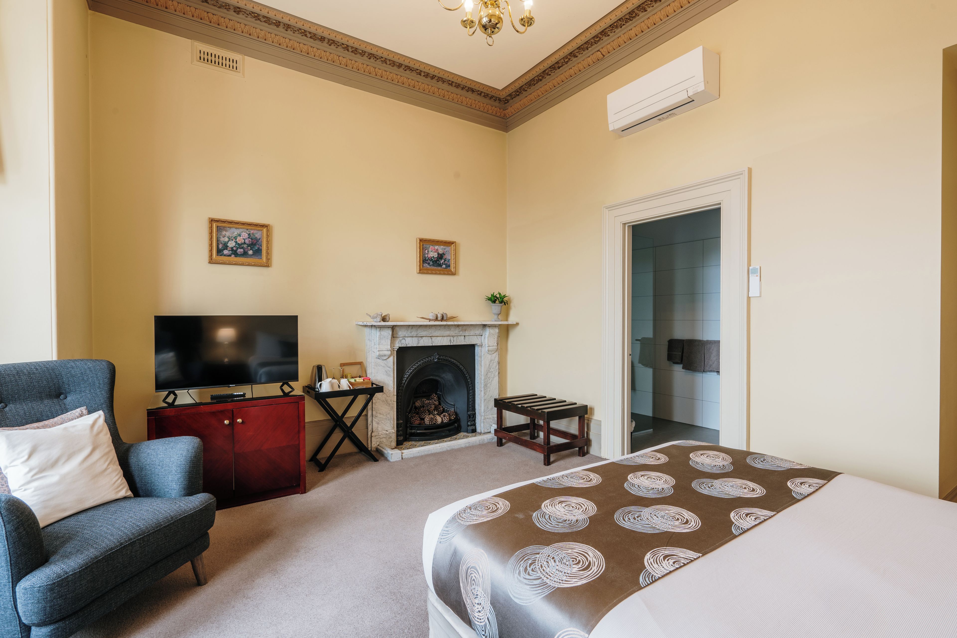 Une chambre d’hôtel équipée d’un lit, d’une télévision, d’une cheminée, d’un fauteuil et d’une porte donnant accès à une salle de bain.