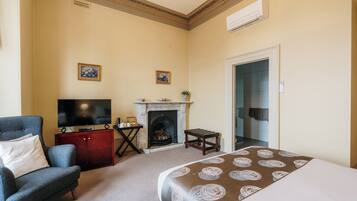 Une chambre d’hôtel équipée d’un lit, d’une télévision, d’une cheminée, d’un fauteuil et d’une porte donnant accès à une salle de bain.