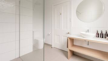 Un bagno moderno con cabina doccia in vetro, water bianco, specchio rotondo e mobile lavabo in legno con lavandino bianco.