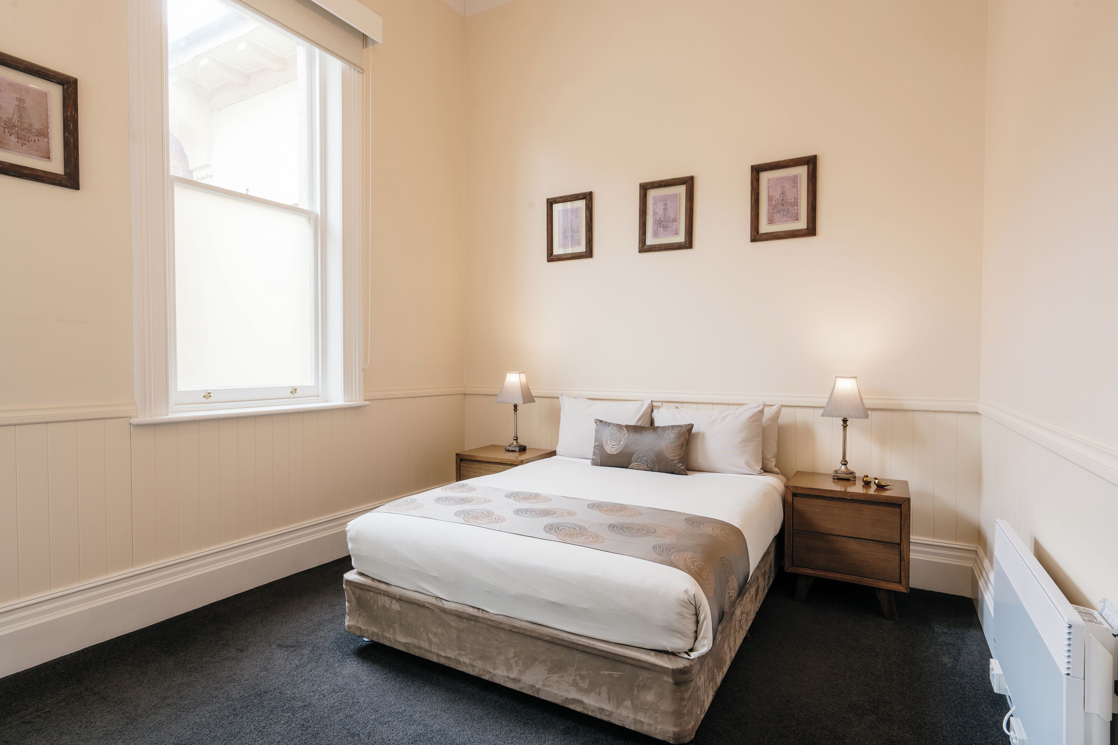 Ein Schlafzimmer mit einem Bett, zwei Nachttischen, einem Fenster und drei gerahmten Bildern an der Wand.