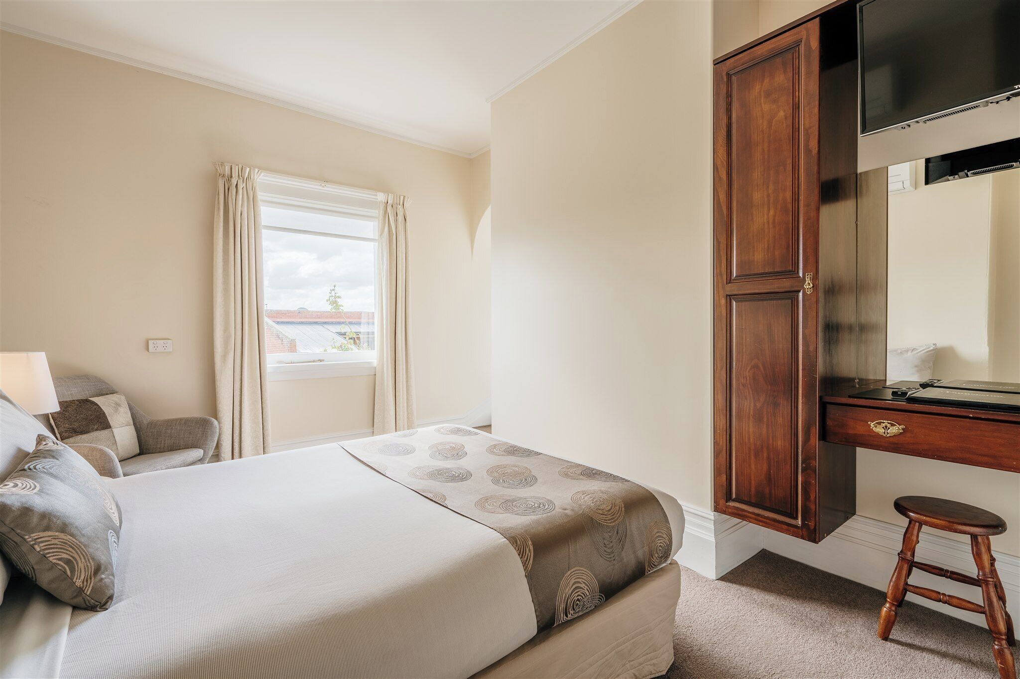 A hotel room with a bed, a desk, a chair, and a wardrobe.