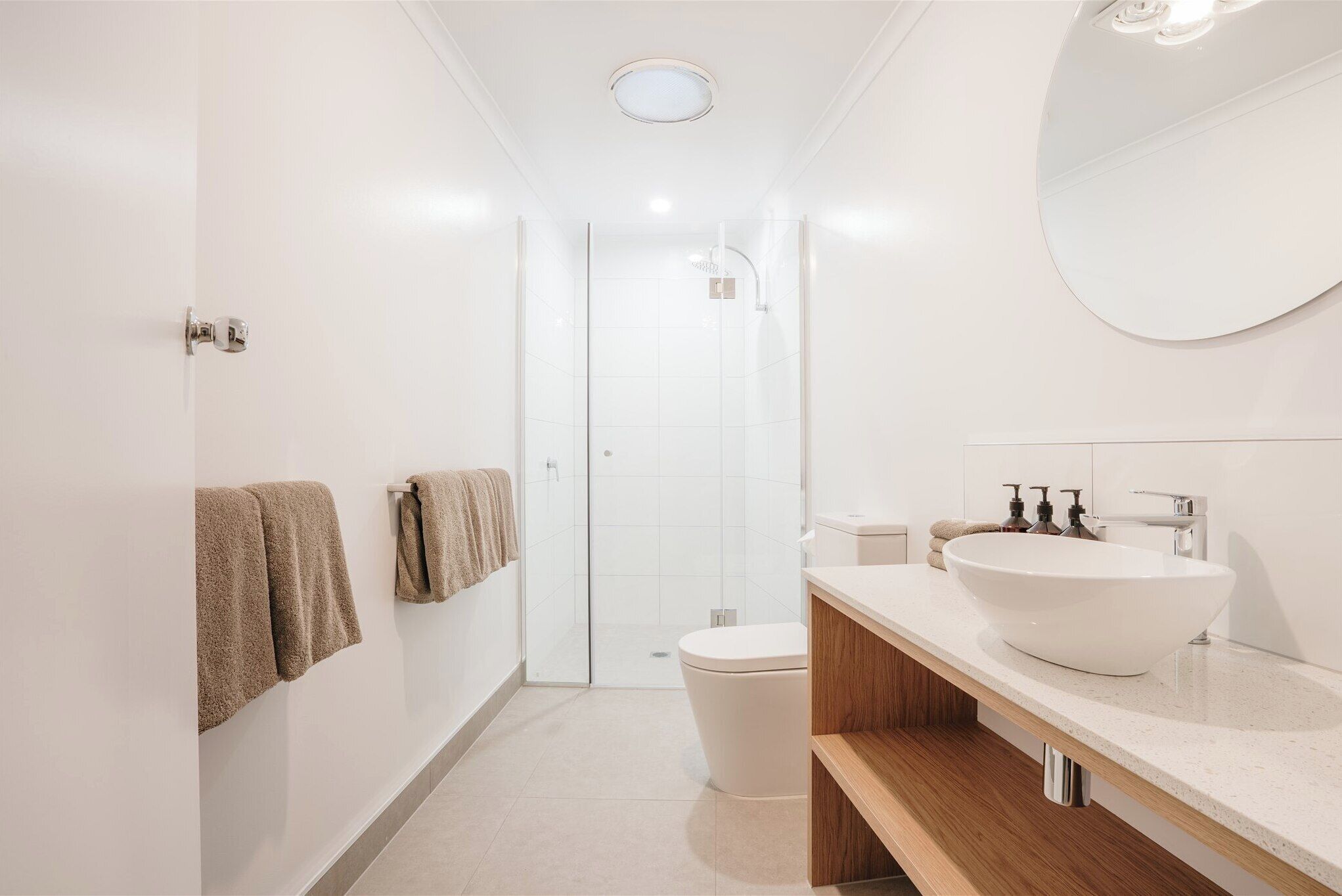 A modern bathroom with a large white sink, a wooden vanity, and a glass shower enclosure.