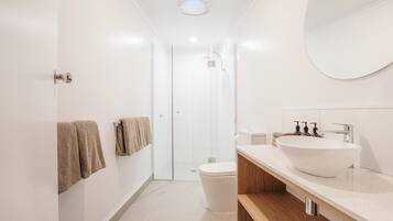 A modern bathroom with a large white sink, a wooden vanity, and a glass shower enclosure.