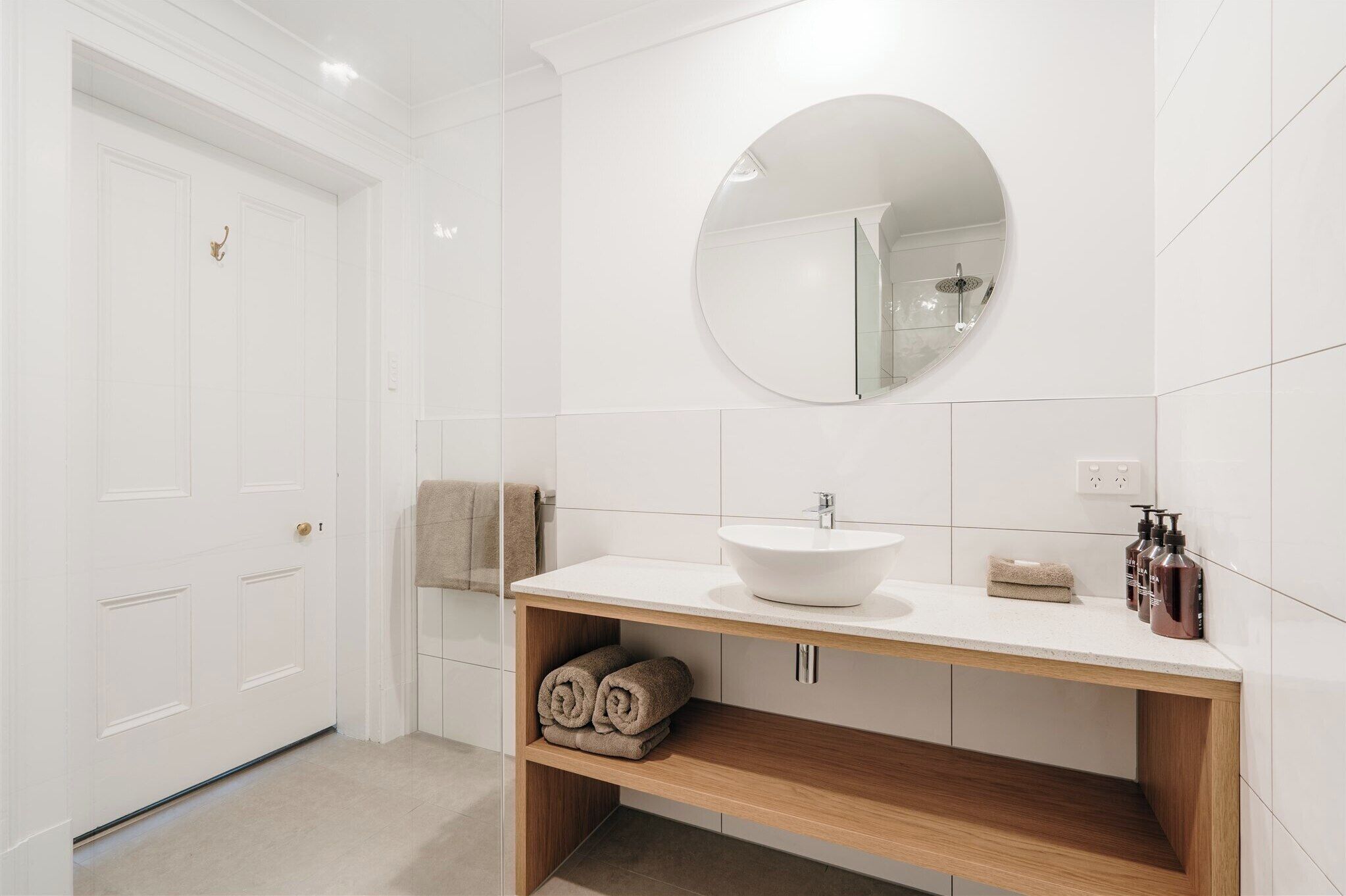 A modern bathroom with a white sink, round mirror, and wooden vanity.