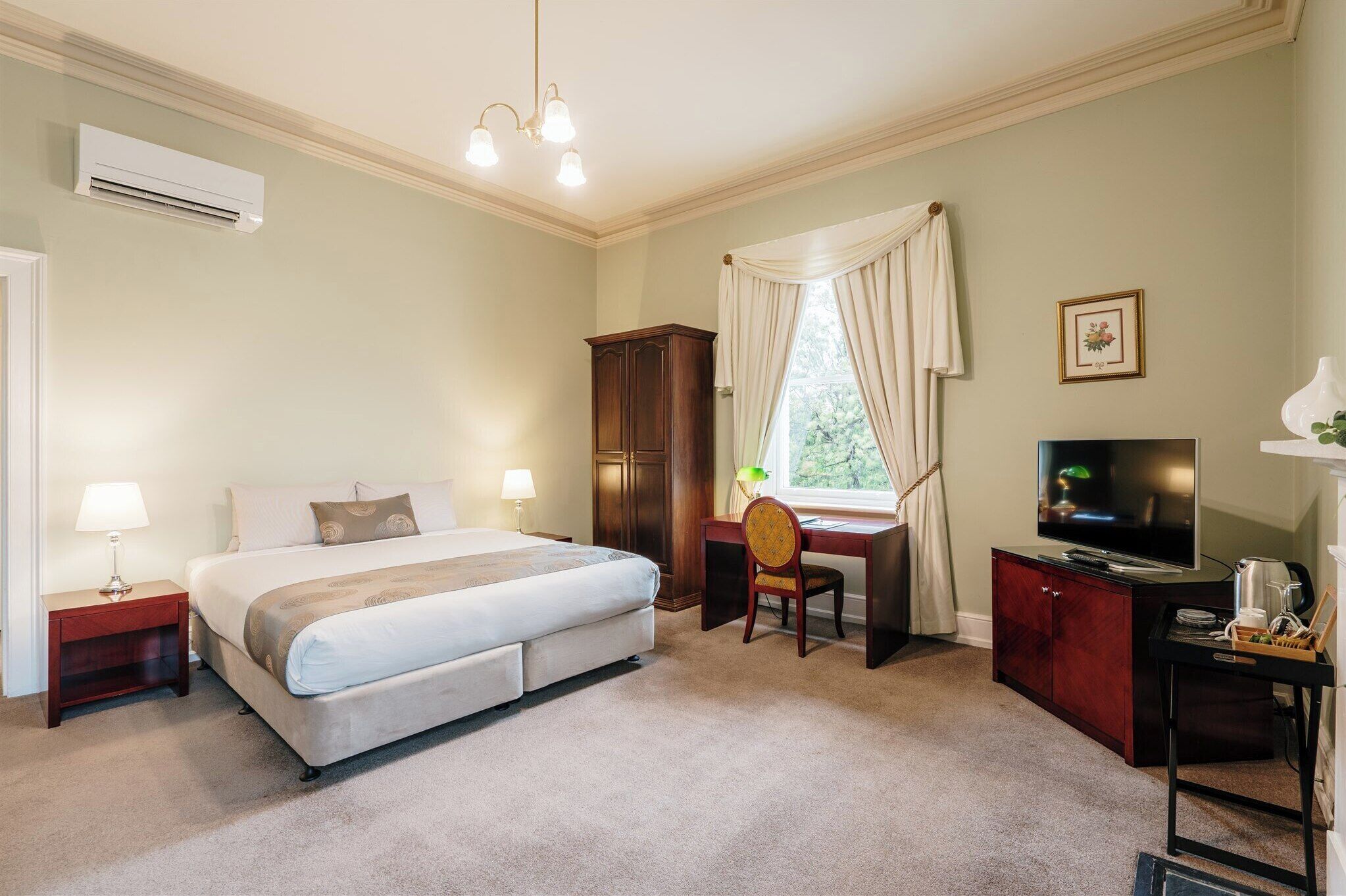 Una habitación de hotel con cama, escritorio, televisión y aire acondicionado.