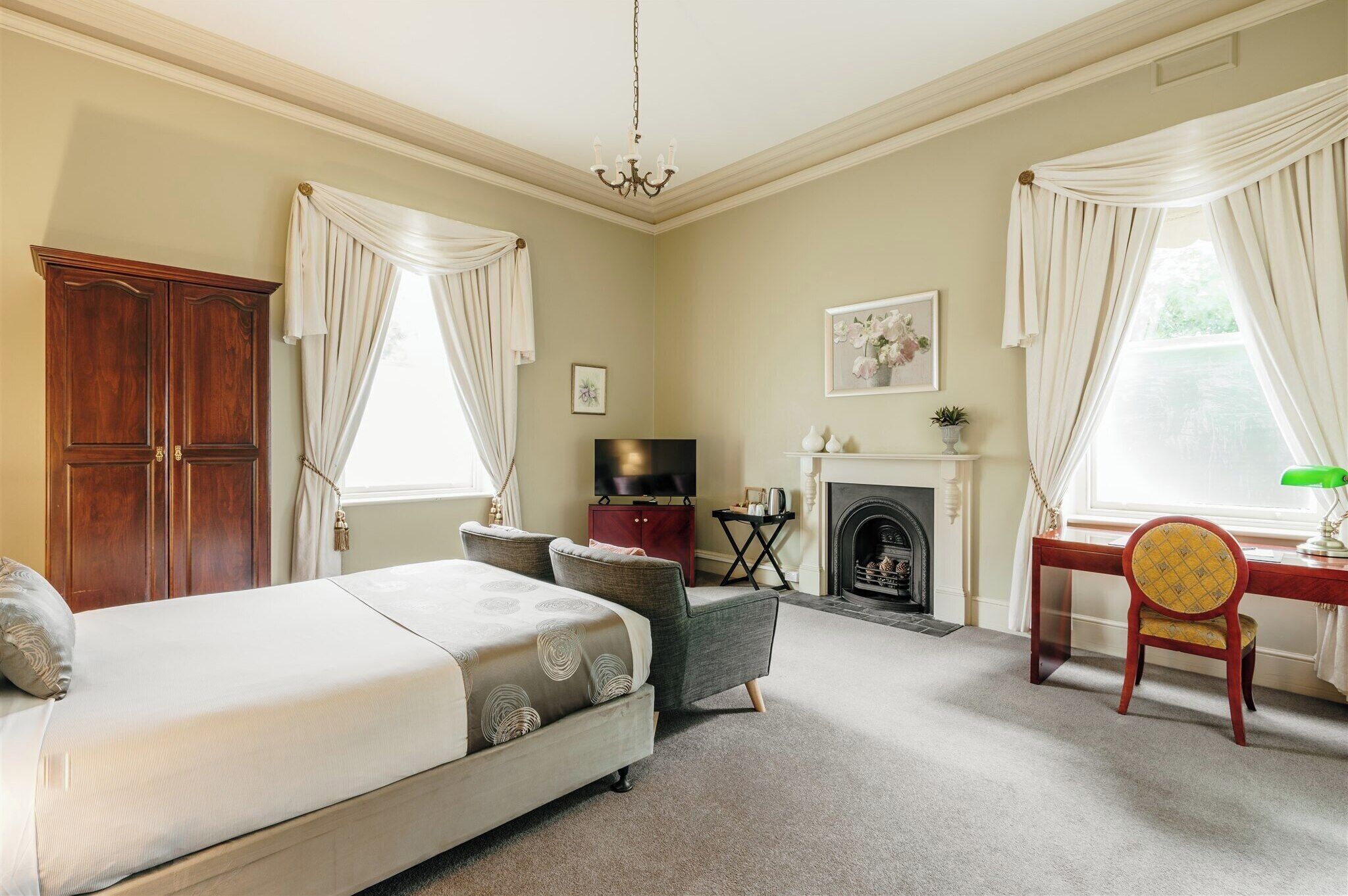 A bedroom with a bed, a desk, a chair, a television, a fireplace, and curtains.