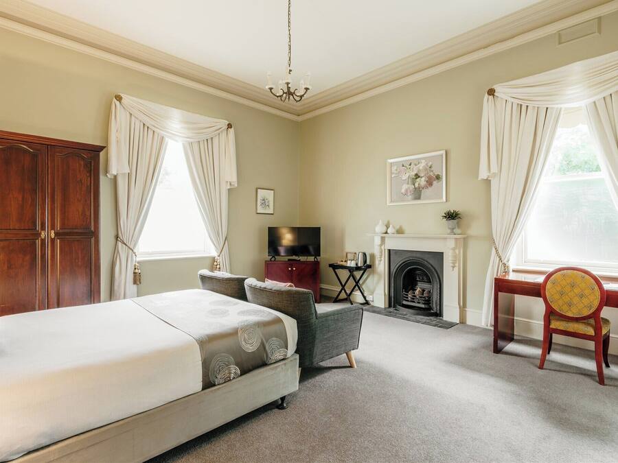 A bedroom with a bed, a desk, a chair, a television, a fireplace, and curtains.