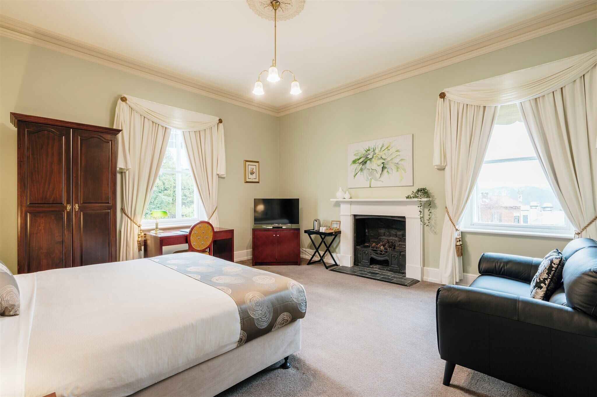 A bedroom with a bed, a dresser, a television, a fireplace, and a sofa.
