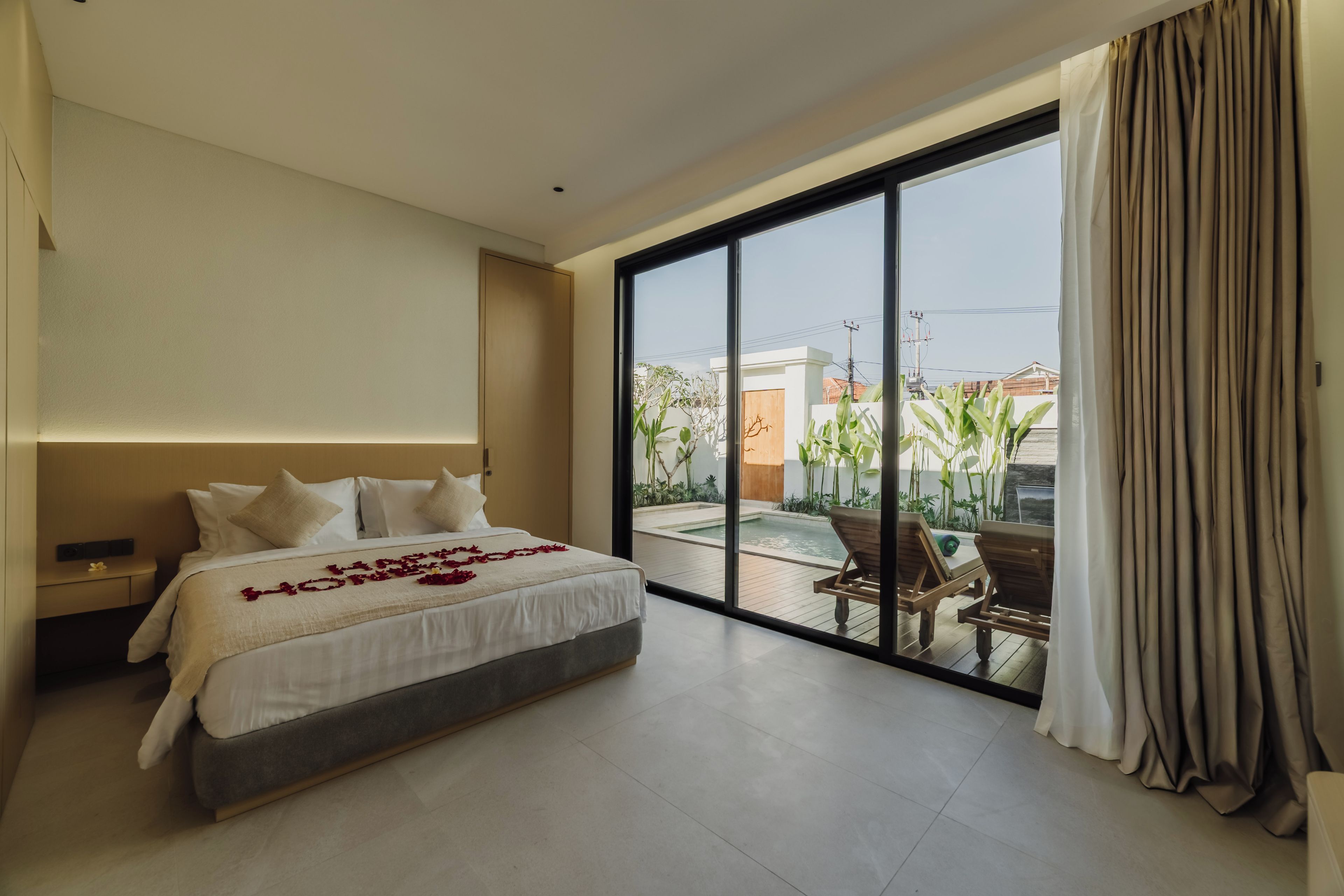 Ein modernes Hotelzimmer mit einem großen Bett, Blick auf einen Pool und Außenbereich sowie einer Schiebetür.