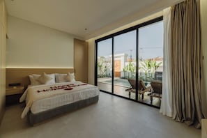 A modern hotel room with a large bed, a view of a pool and outdoor area, and a sliding glass door. - Gracia Bali Villas & Apartment (Seminyak)
