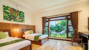 Een hotelkamer met twee bedden, een bureau en een groot raam met uitzicht op groen.