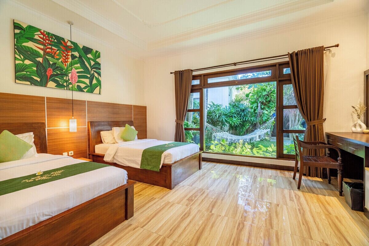 A hotel room with two beds, a desk, and a large window with a view of greenery.