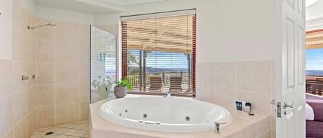 A modern bathroom with a large bathtub, a shower area, and a window with blinds.